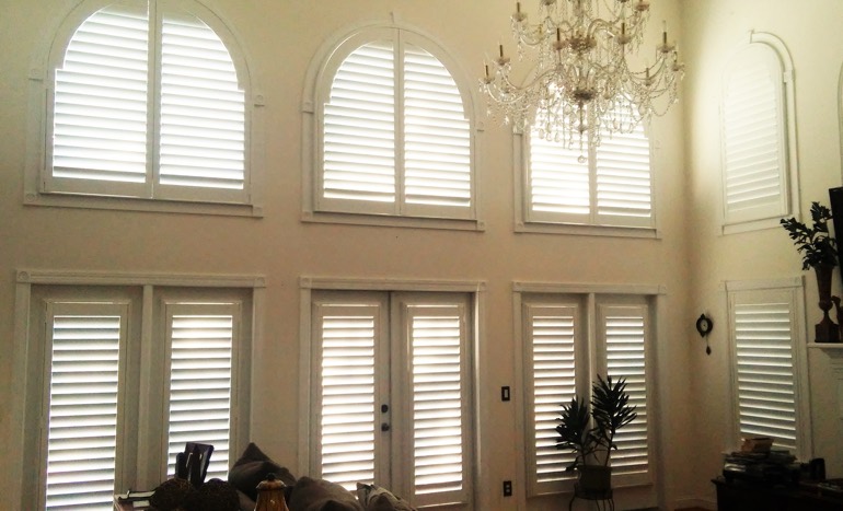 Family room in two-story Las Vegas house with plantation shutters on high ceiling windows.