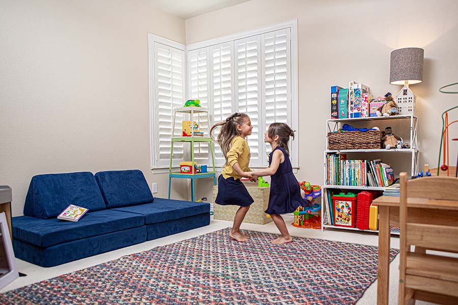 Durable and cordless, Polywood shutters are safe window treatments for any child's room. Two girls playing in a toy room with Polywood shutters on the windows