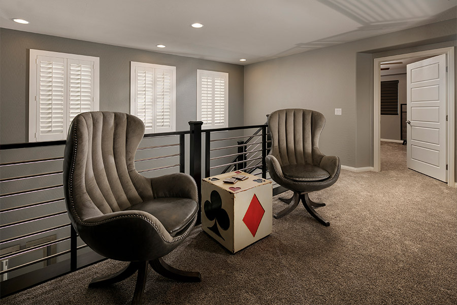 A white window treatment on a darker wall can do wonders for your Las Vegas home. two chairs and a small dice-themed table in front of a stairwell with shuttered covered small windows