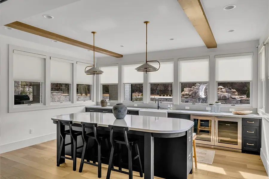 Get a cost estimate for motorized shades during your Sunburst consultation. White motorized roller shades on windows in a stunning kitchen and dining area