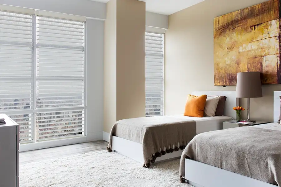 Many shade styles, such as these sheer shades, can be motorized. Sheer shades on tall windows in a bedroom with views of the city